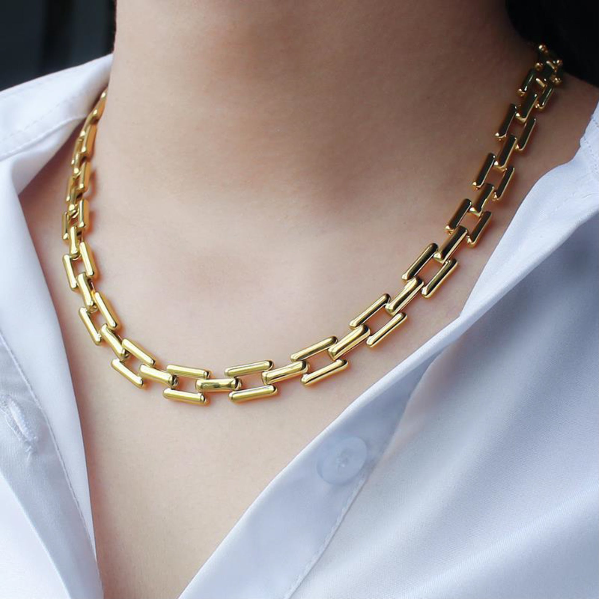 Gold chain necklace worn by a person with a white shirt background