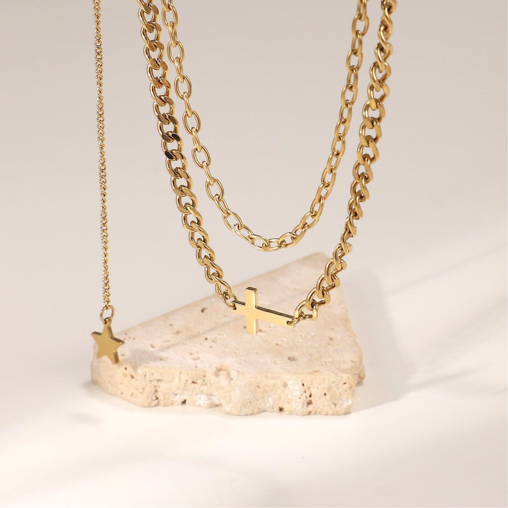 Two gold necklaces with pendants on a light stone surface