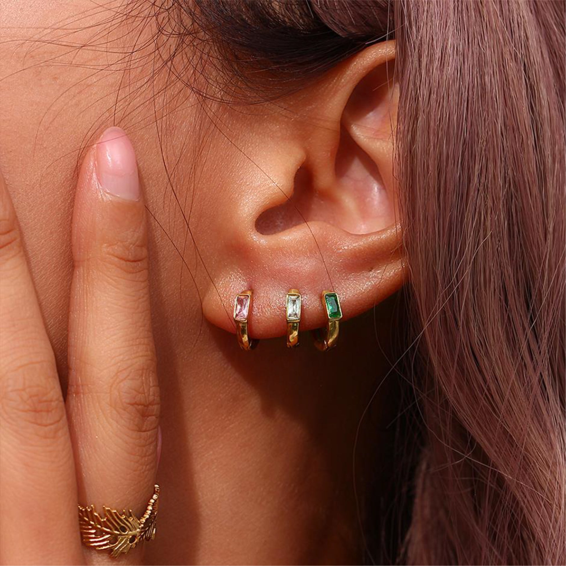 Close-up of an ear wearing multiple earrings with a hand touching the side of the head.