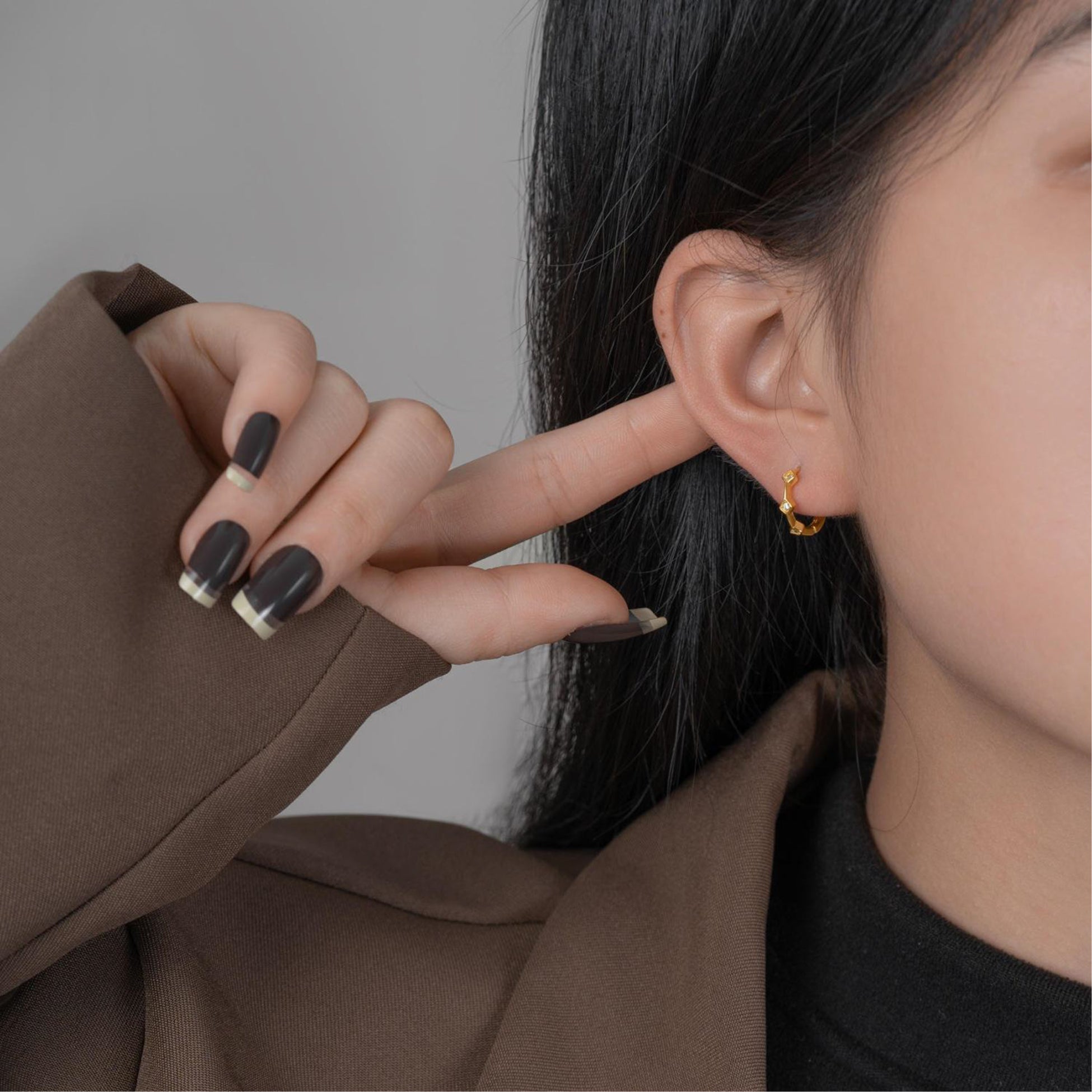 Close-up of a person wearing a gold earring with a neutral background