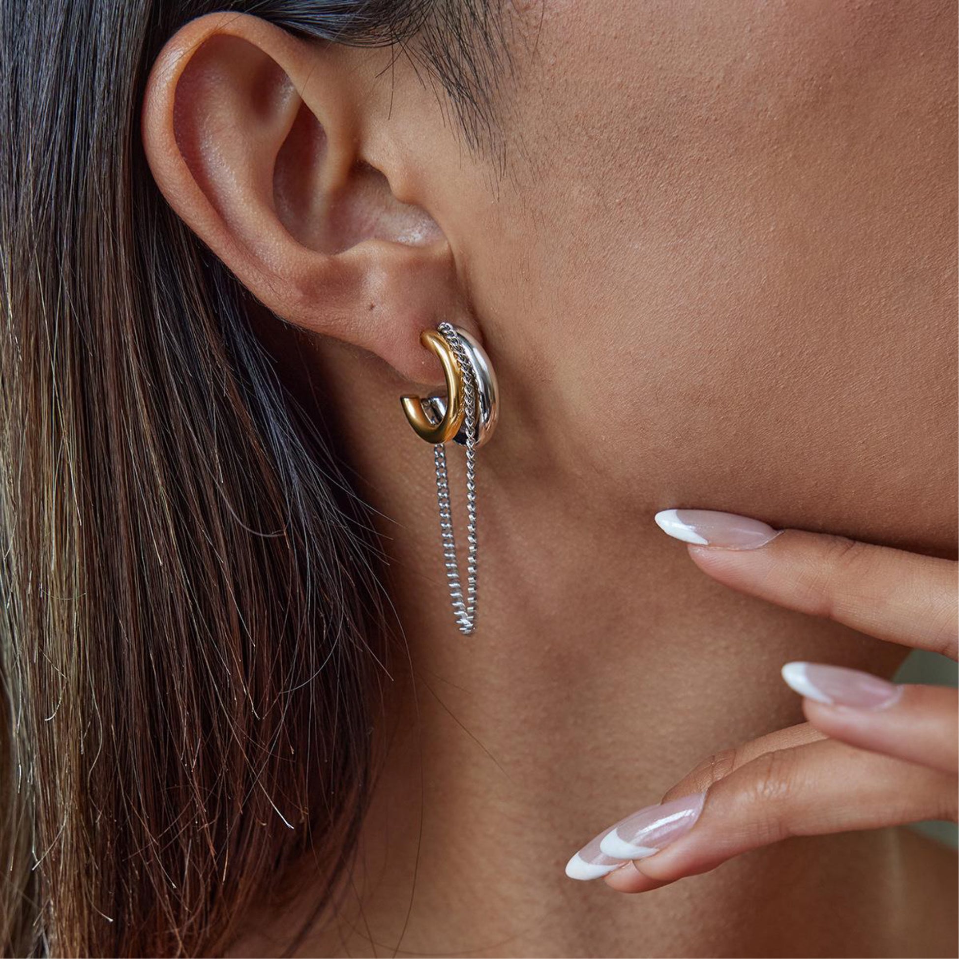 Close-up of an ear wearing a gold and silver earring with a hand touching the skin.