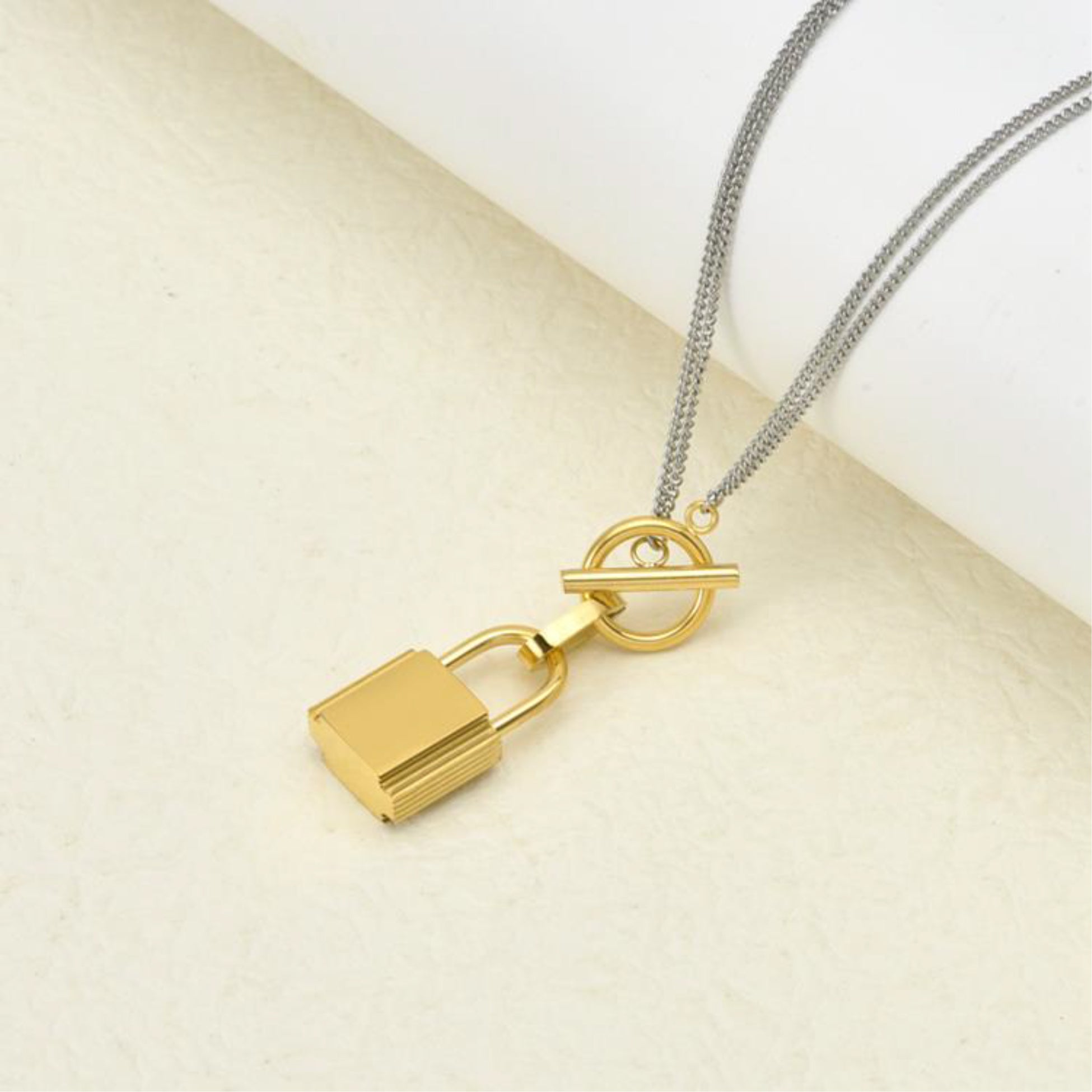 Gold lock pendant on a silver chain against a beige background