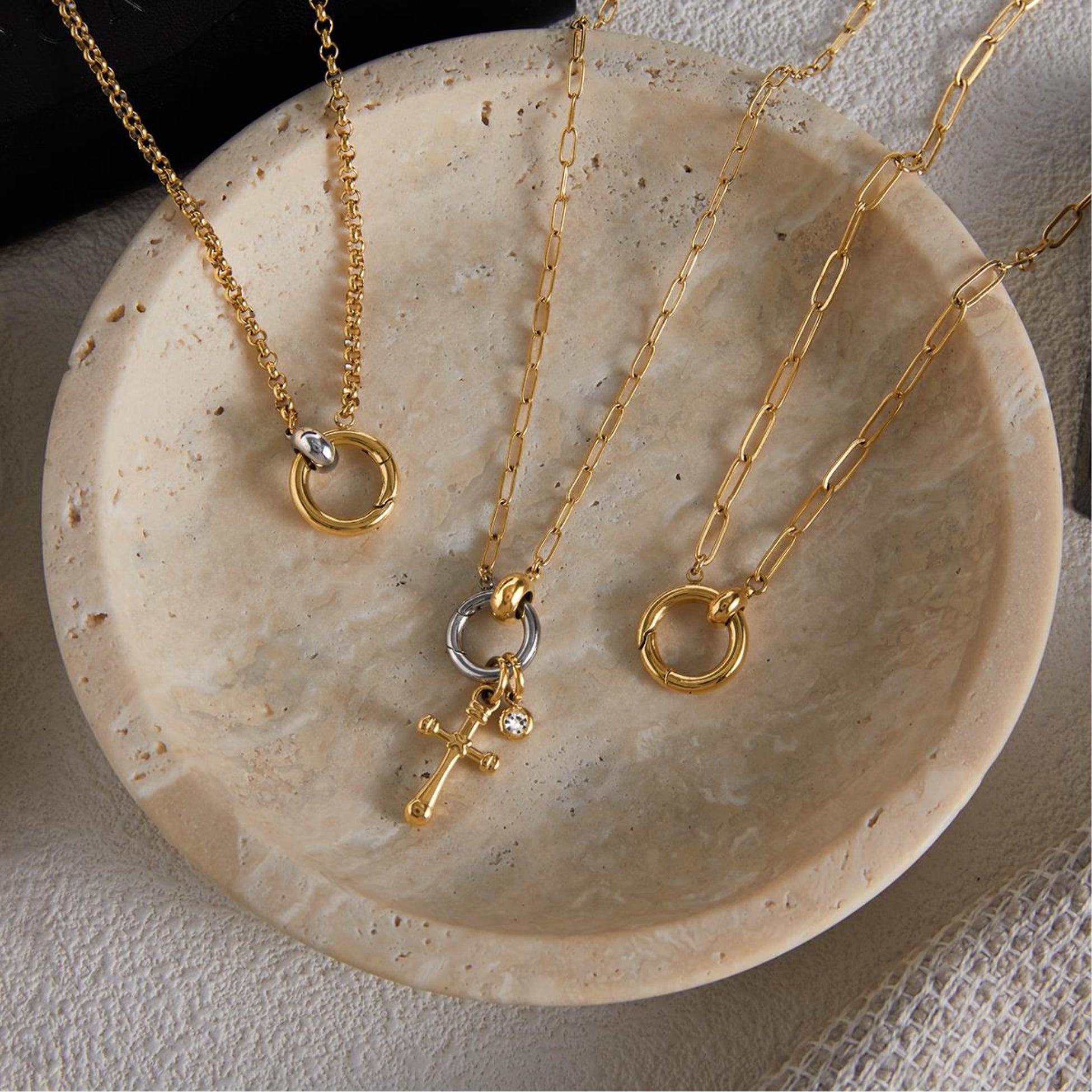 Three gold necklaces with pendants on a beige stone surface