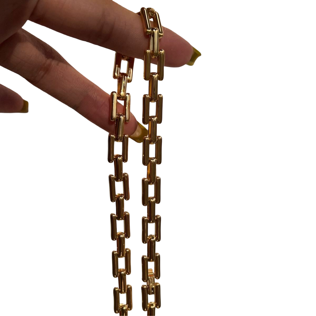 Gold chain necklace held by a hand on a white background