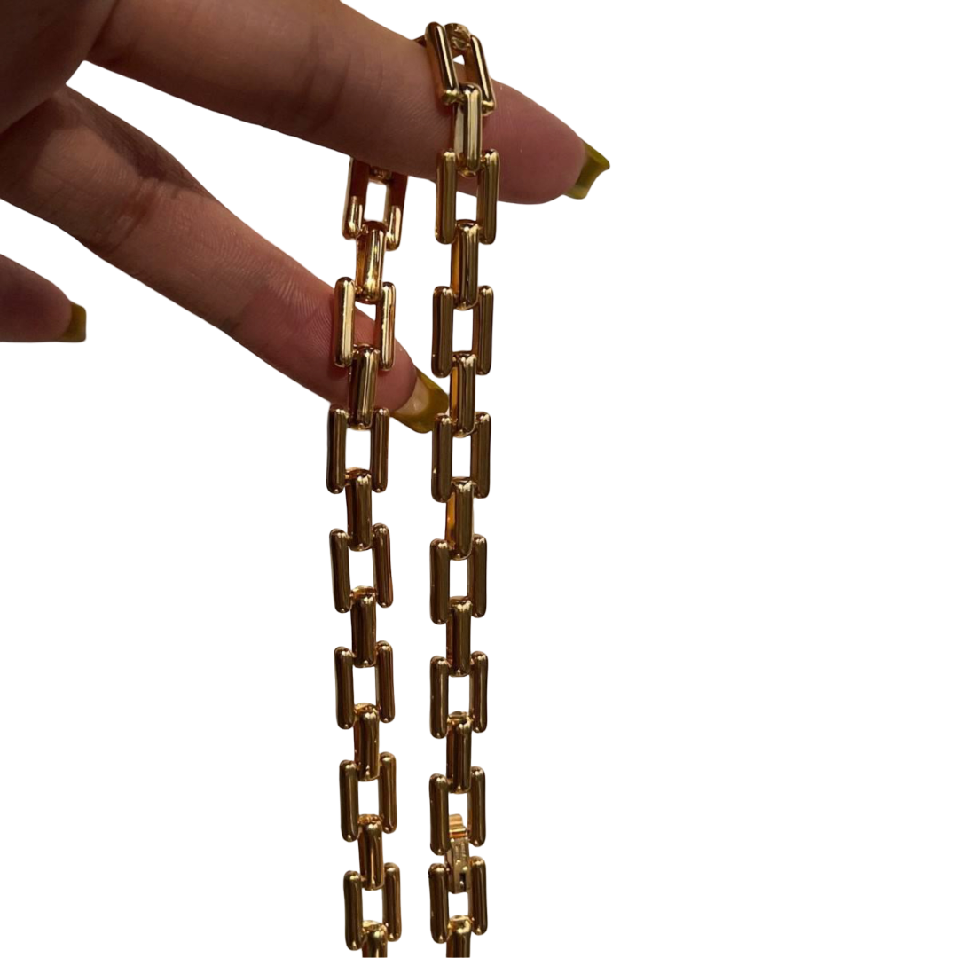Gold chain necklace held by a hand on a white background