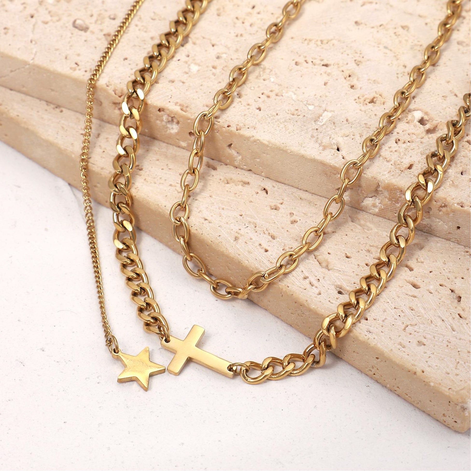 Three gold chains with star and cross pendants on a light wooden surface.