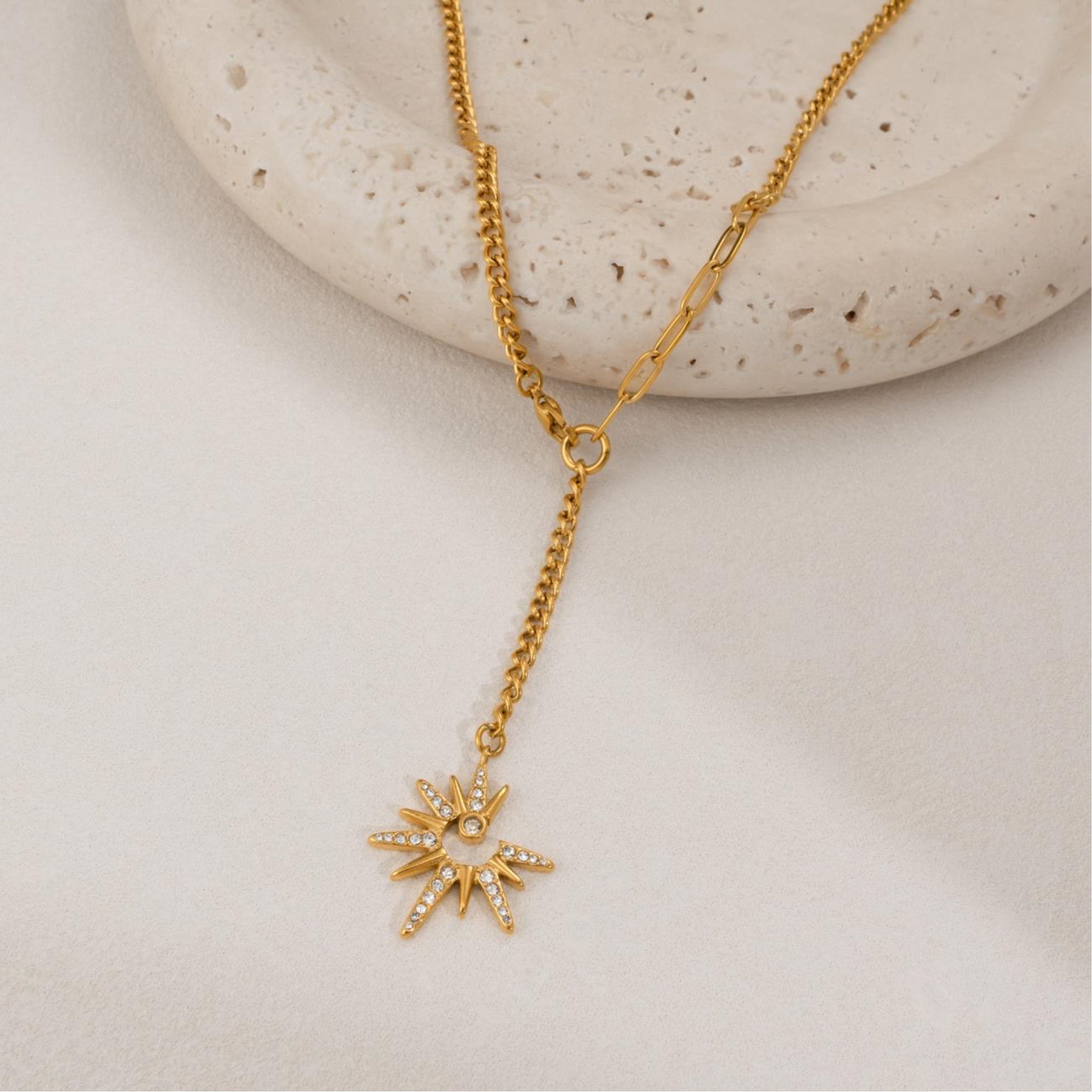 Gold necklace with a star-shaped pendant on a light stone surface