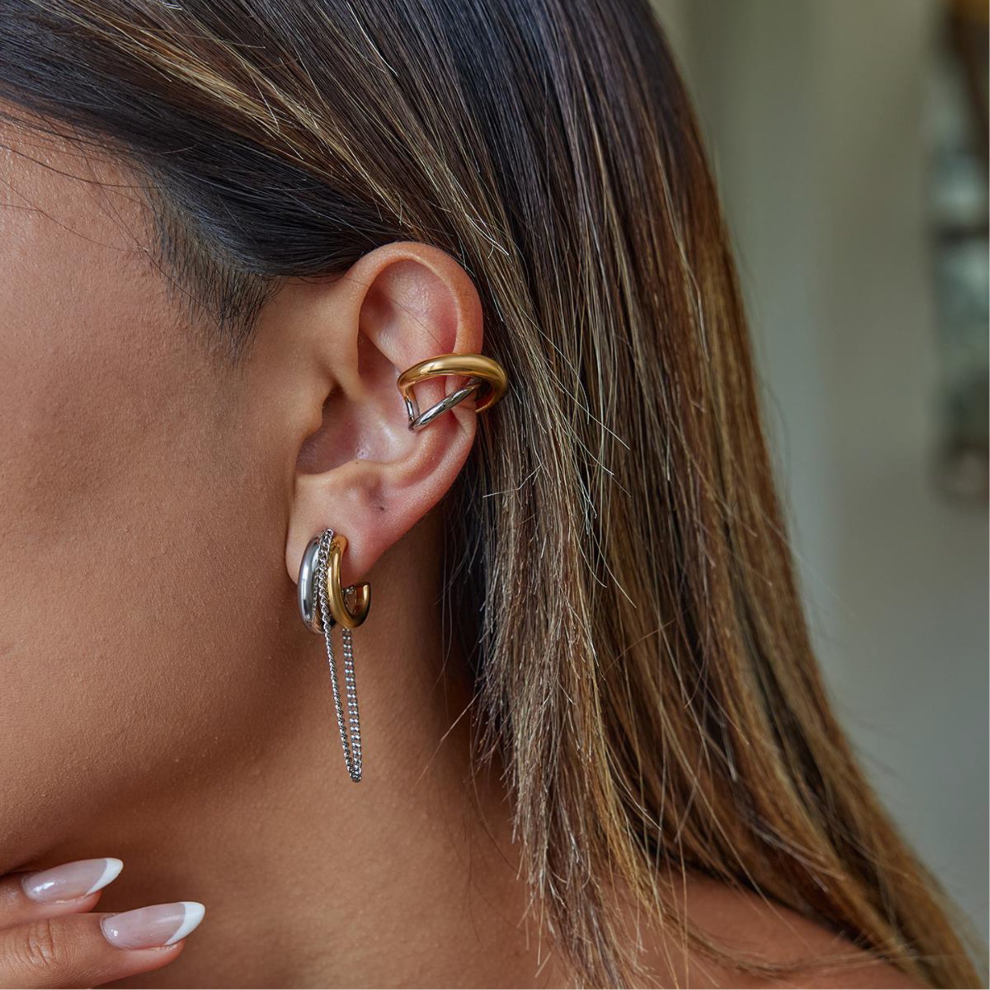 Close-up of a person wearing gold hoop earrings with a blurred background