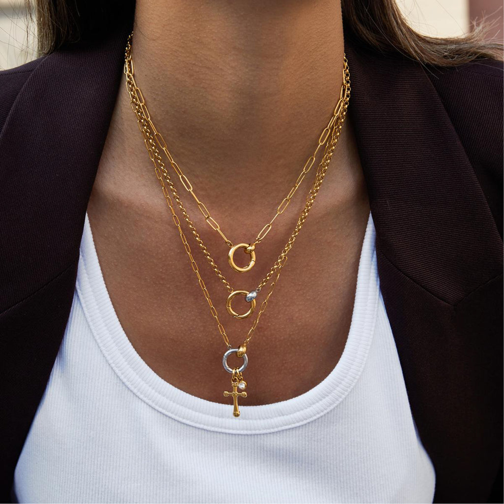 Close-up of a person wearing multiple gold necklaces with a plain background