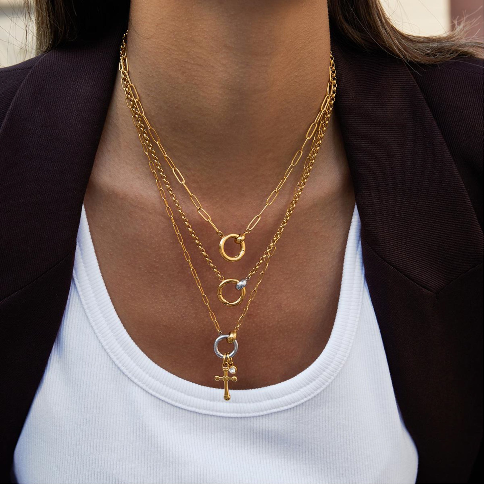 Close-up of a person wearing multiple gold necklaces with a plain background