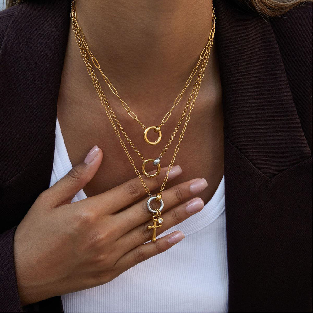Person wearing multiple gold necklaces with intricate pendants, holding one necklace with their hand.